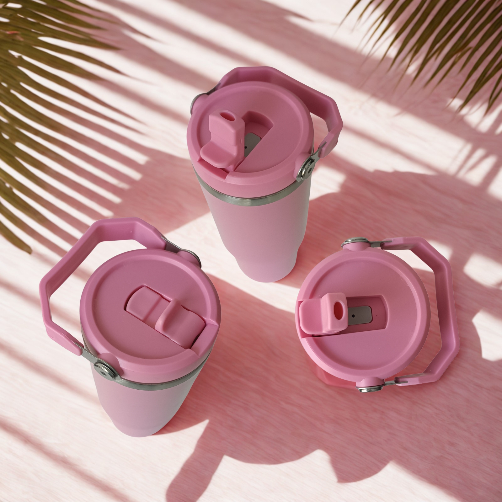 Top view of three Rose Dust tumblers showing closed lid, open straw, and spout details under palm leaf shadows