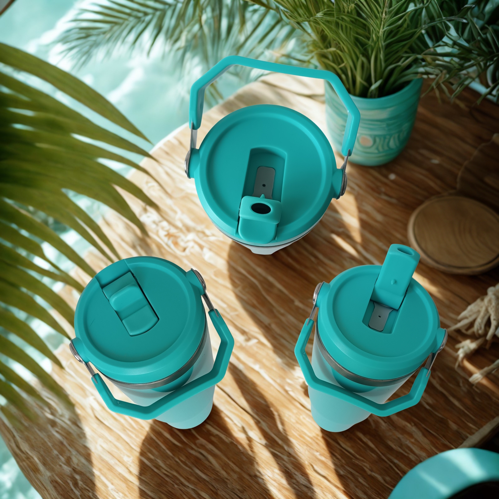 Top-down view of three Tropical Turquoise tumblers on a wood table by the water, with two straws up and one closed lid
